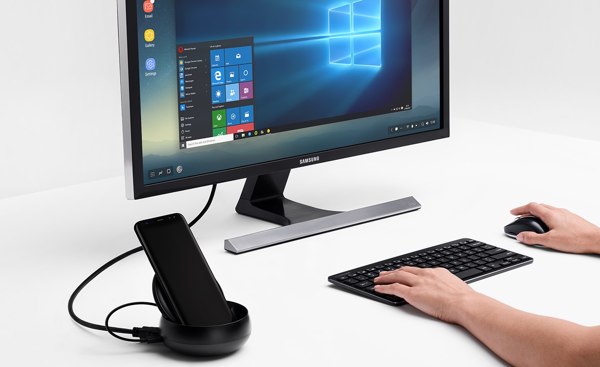 Vaizdas, kuriame naudojama klaviatūra ir pelė priešais monitorių ir juodas „Galaxy S8“, prijungtas prie „Samsung DeX Station“.