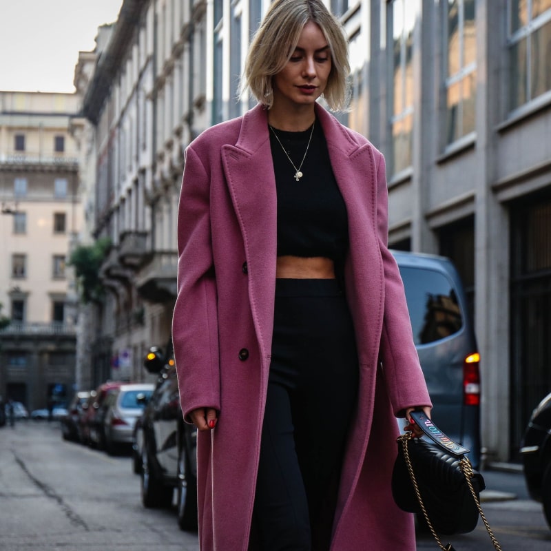 женщина в розовом пальто идет по улице