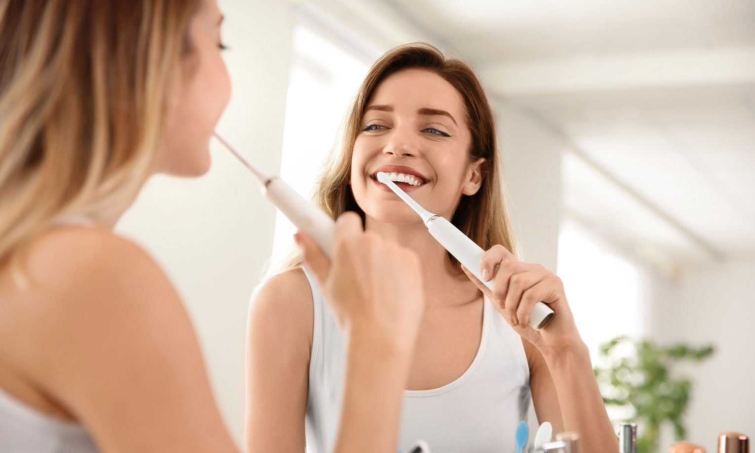 девушка чистит зубы электрической зубной щеткой перед зеркалом