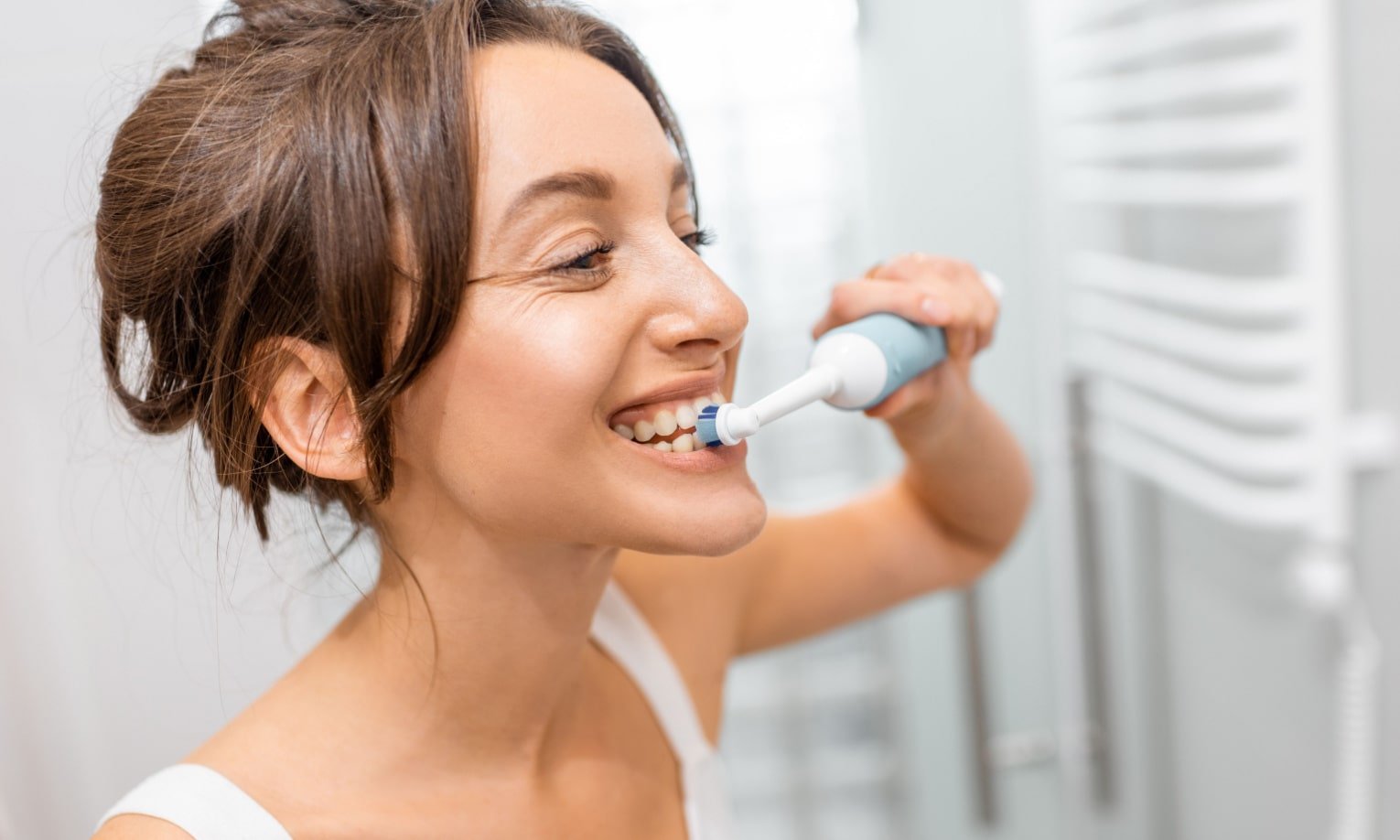 nainen pesee hampaansa sähköhammasharjalla
