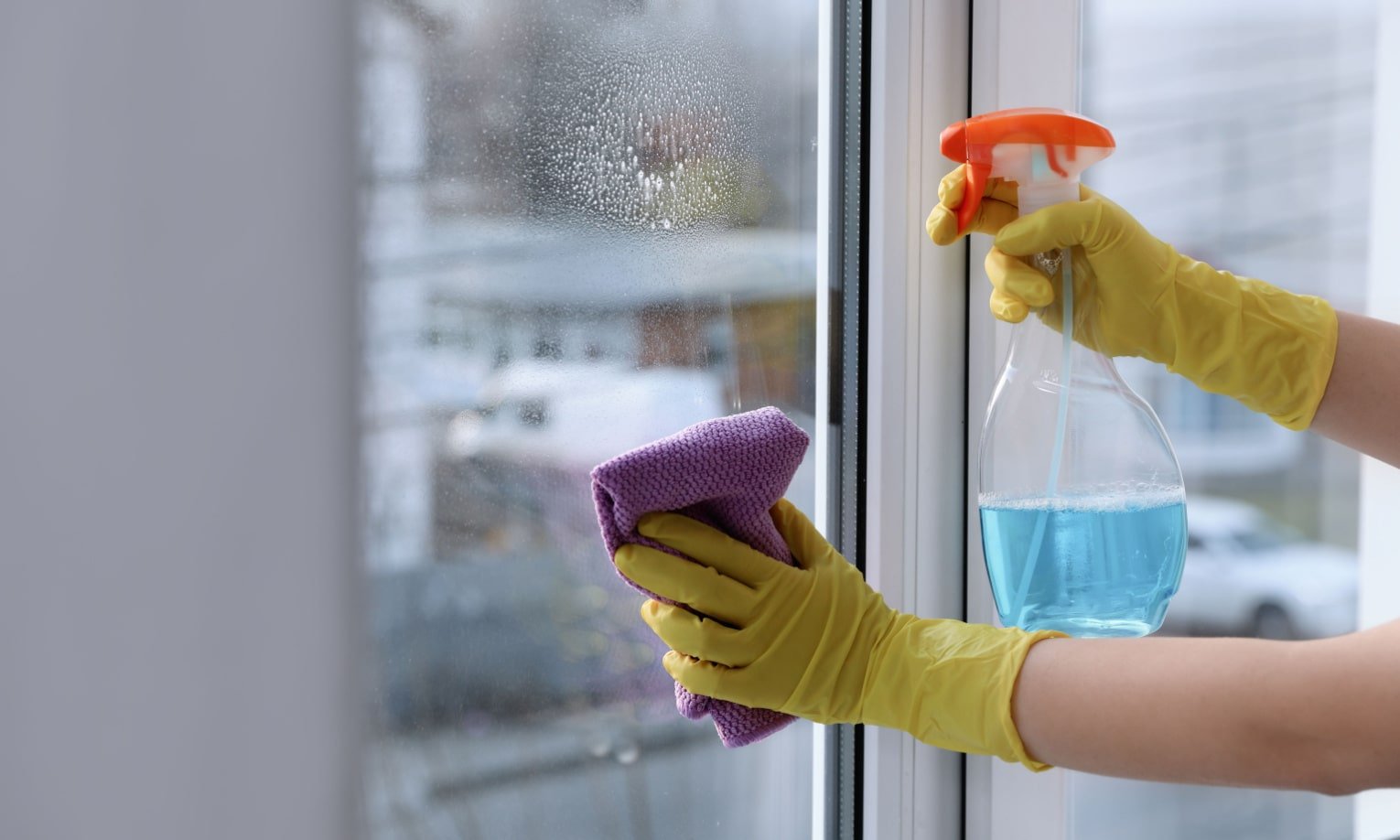 женщина моет окно средством и салфеткой из микрофибры