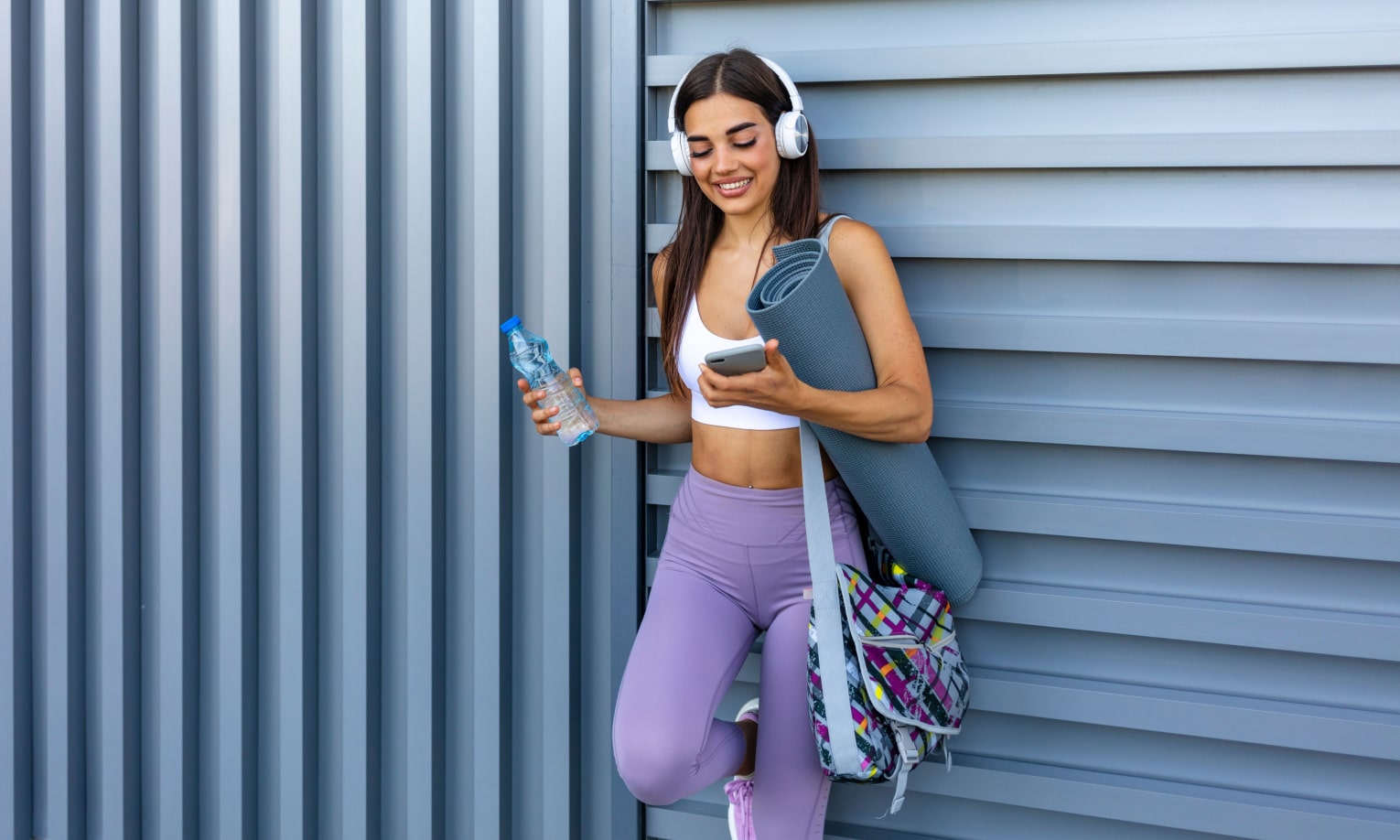 девушка в наушниках с ковриков для йоги и телефоном в руках