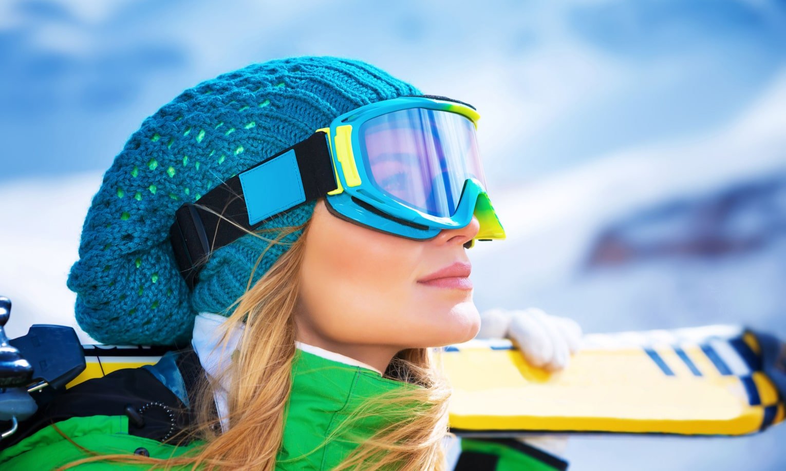 девушка в горнолыжных очках с лыжами на плече
