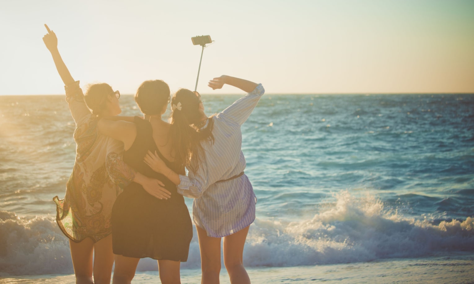 подруги фотографируются с палкой для селфи на берегу моря