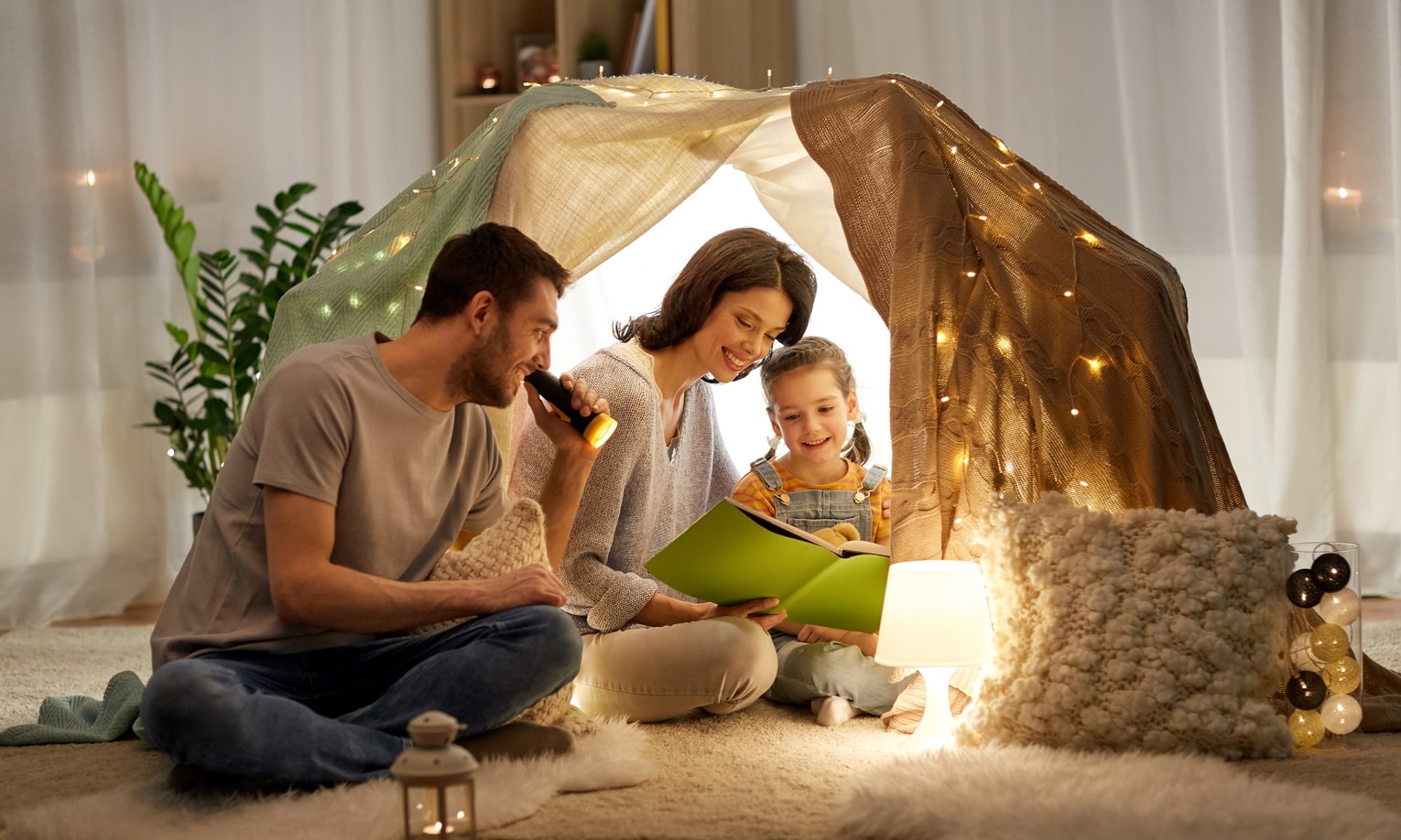 папа и мама читают дочке книгу в палатке