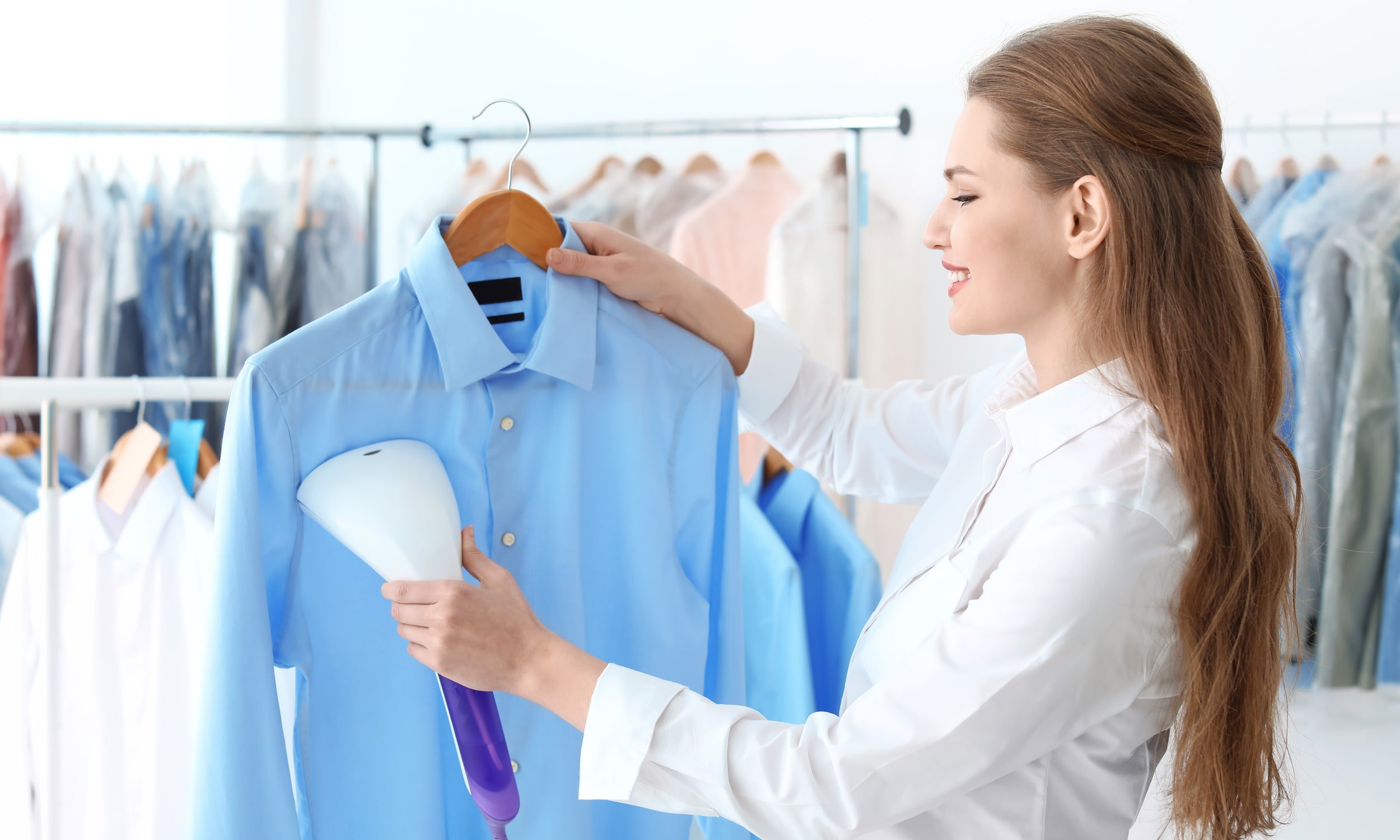 девушка гладит рубашку голубого цвета отпаривателем