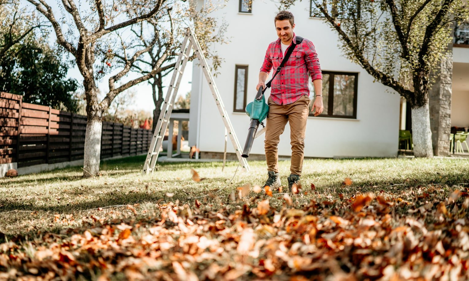 мужчина убирает листья во дворе с помощью воздуходувки