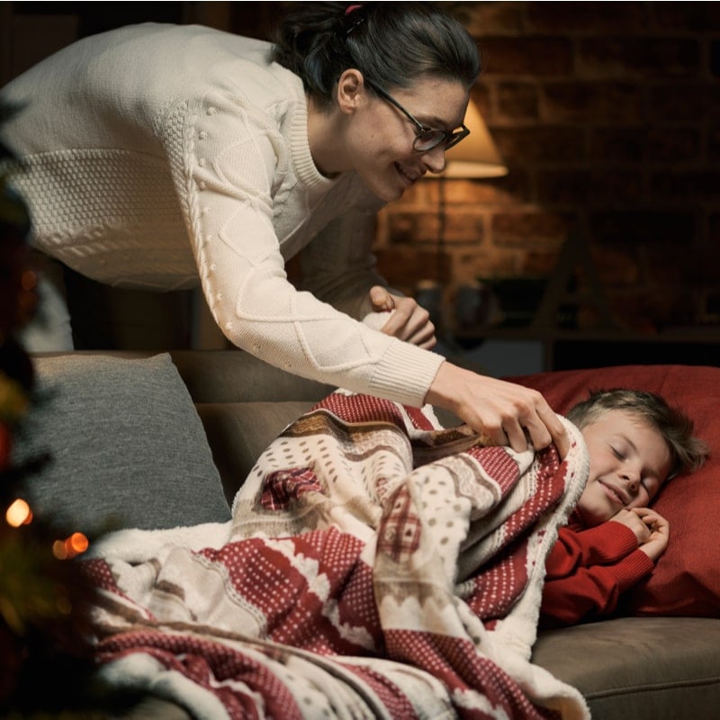 мама укрывает спящего мальчика рождественским пледом