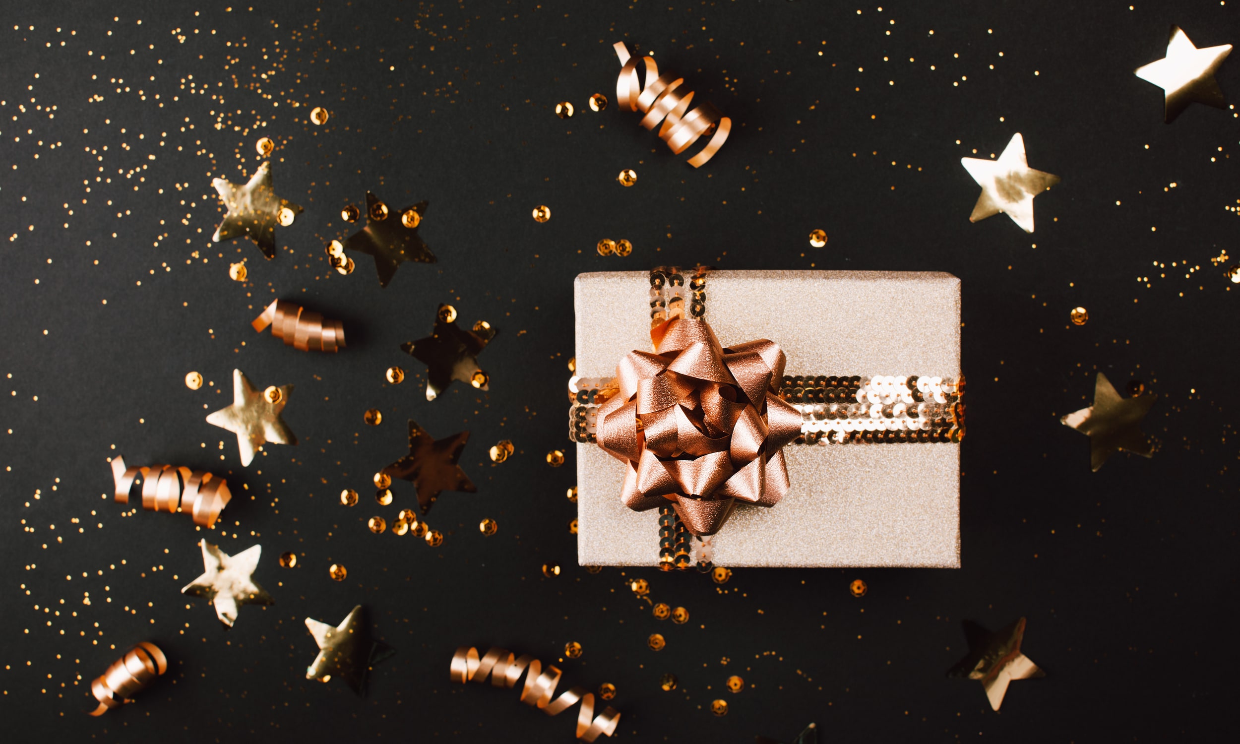 graziai supakuota auksine kaledine dovana ant tamsaus stalo su konfeti
