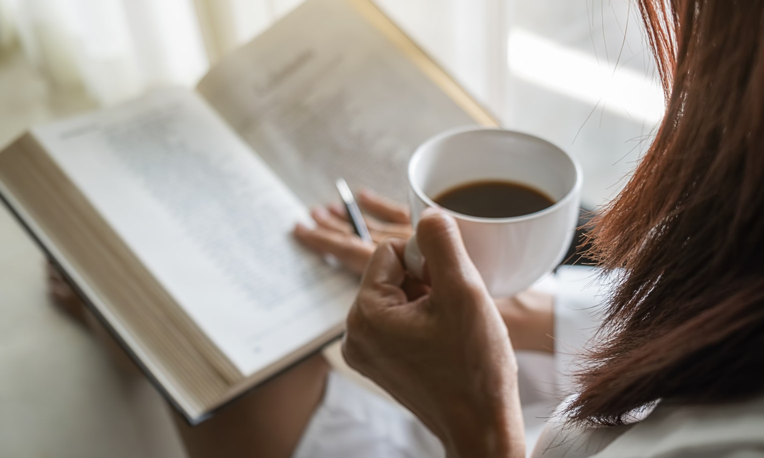 moteris skaito knyga ir geria kava
