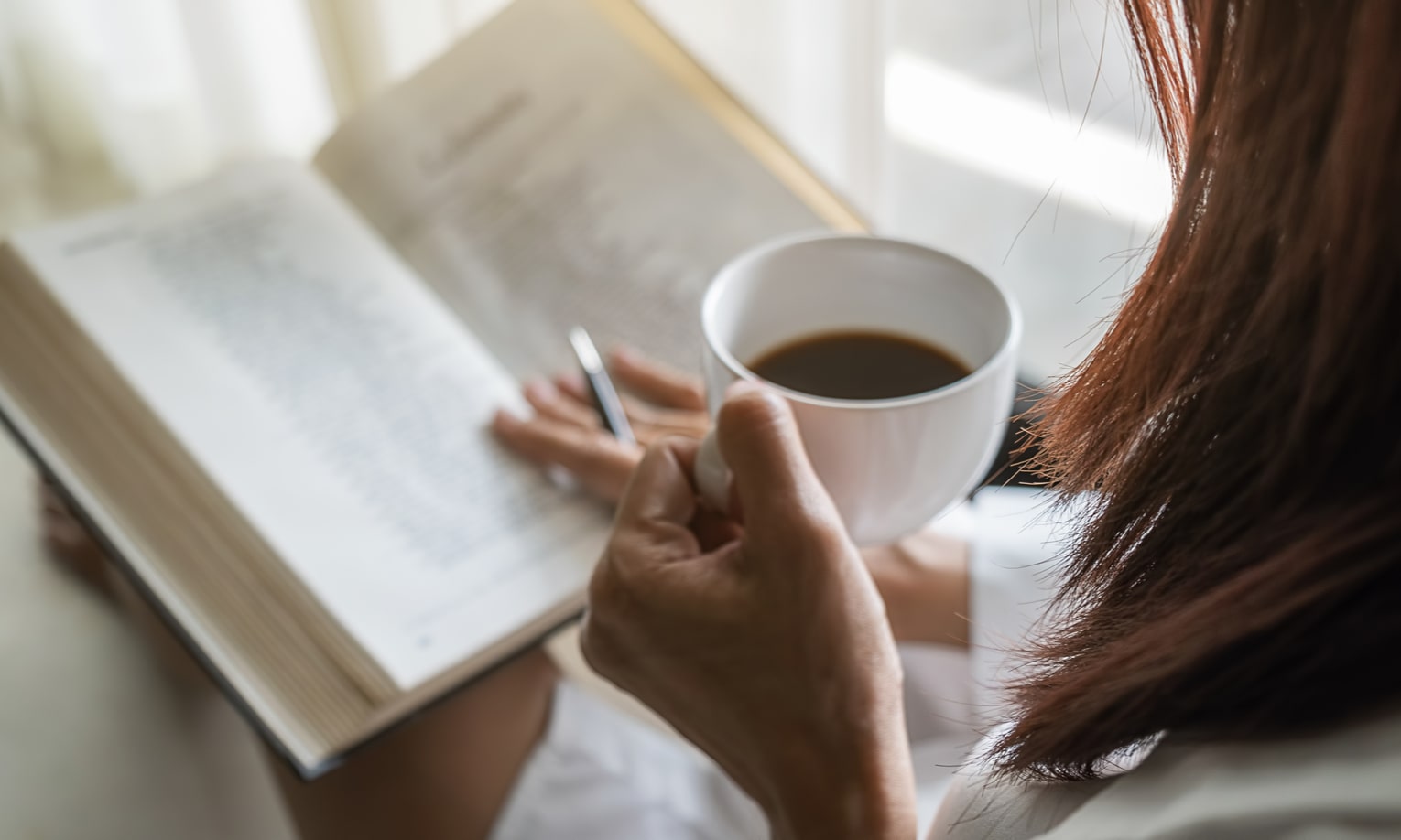 женщина читает книгу, держа чашку кофе