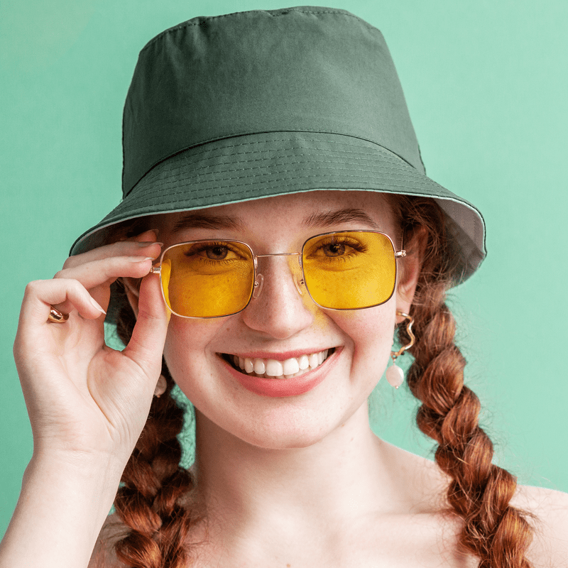punutiste, rohelise mütsi ja kollaste prillidega tüdruk kaamera ees naeratades