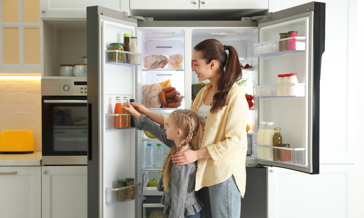 мама и дочка достают продукты из двухдверного холодильника