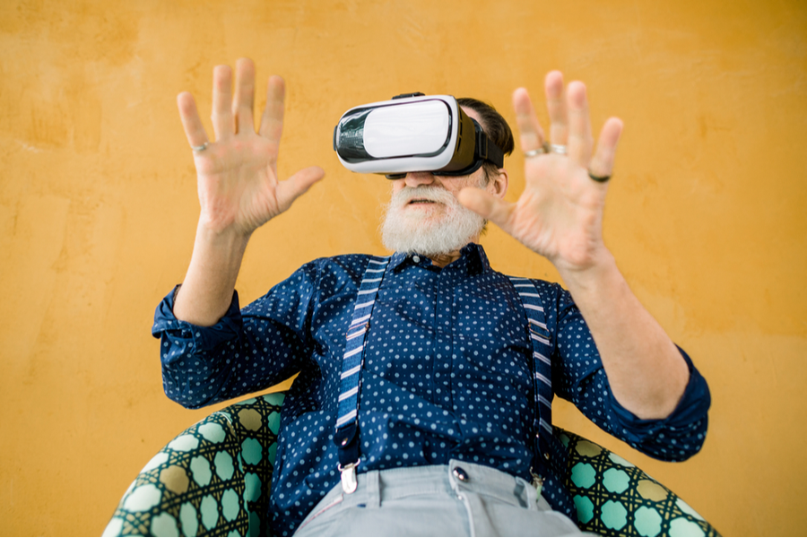 vyras naudojasi virtualios realybes akiniais sededamas ant sofos