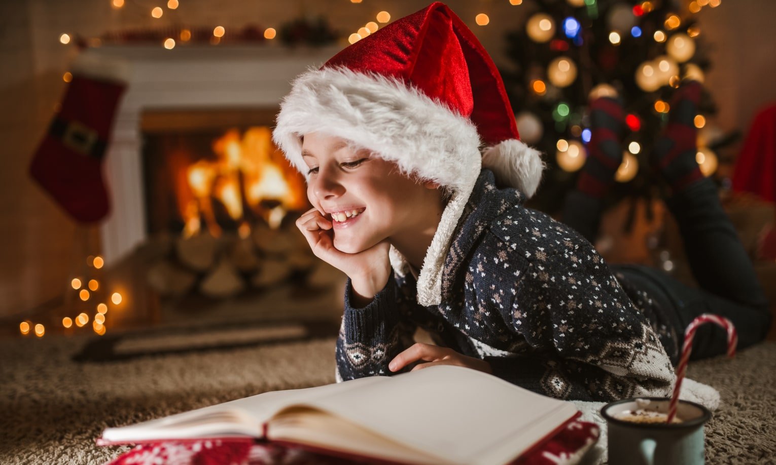 мальчик в рождественской одежде читает книгу у камина