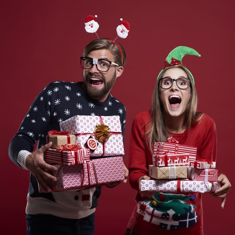 пара в рождественских свитерах с подарками в руках