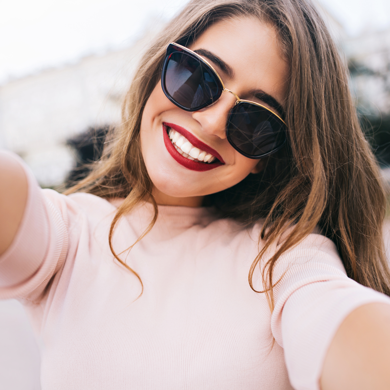 laiminga mergina ilgais plaukais su akiniais nuo saules pozuoja kamerai