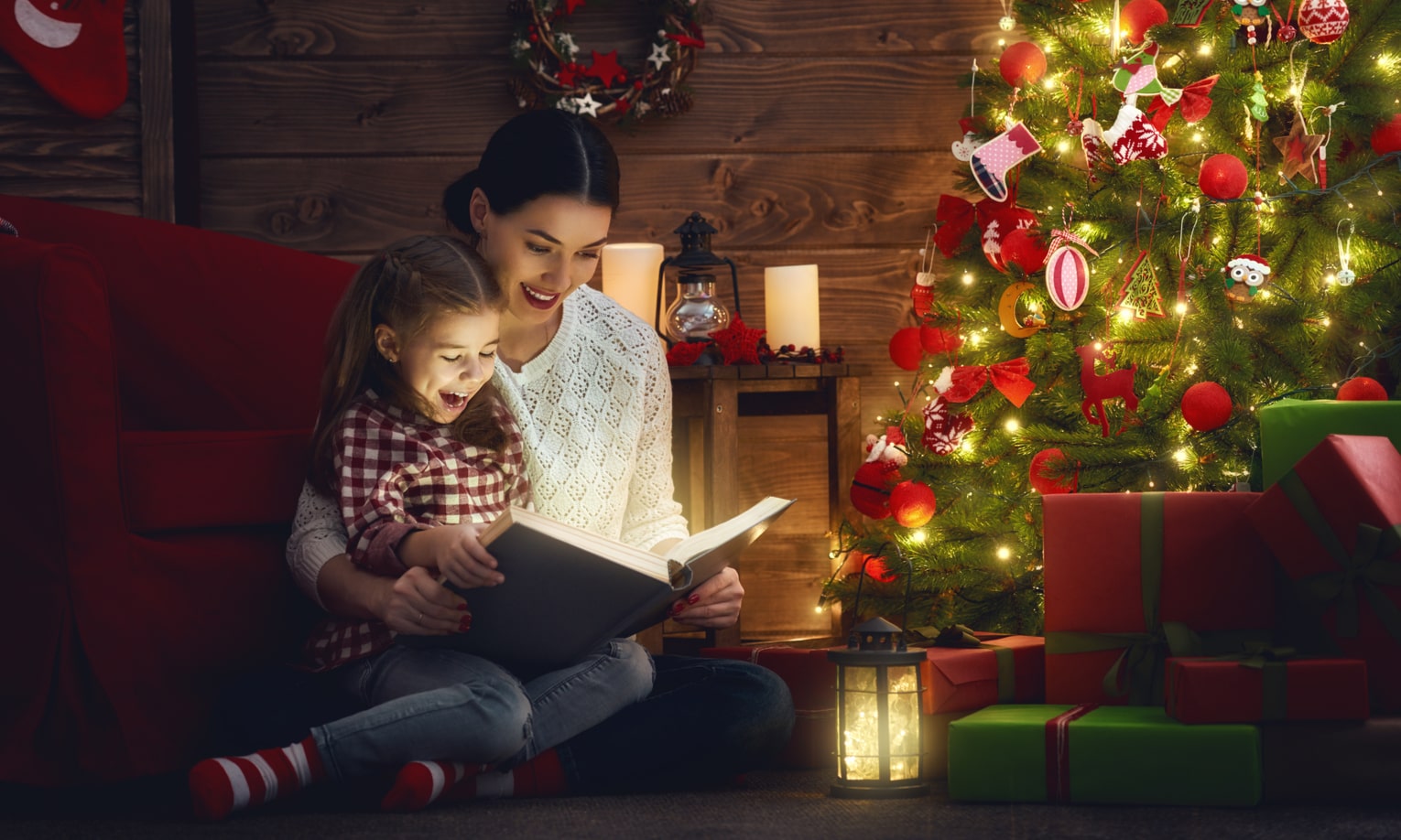 мама с дочкой читают книгу у рождественской елки