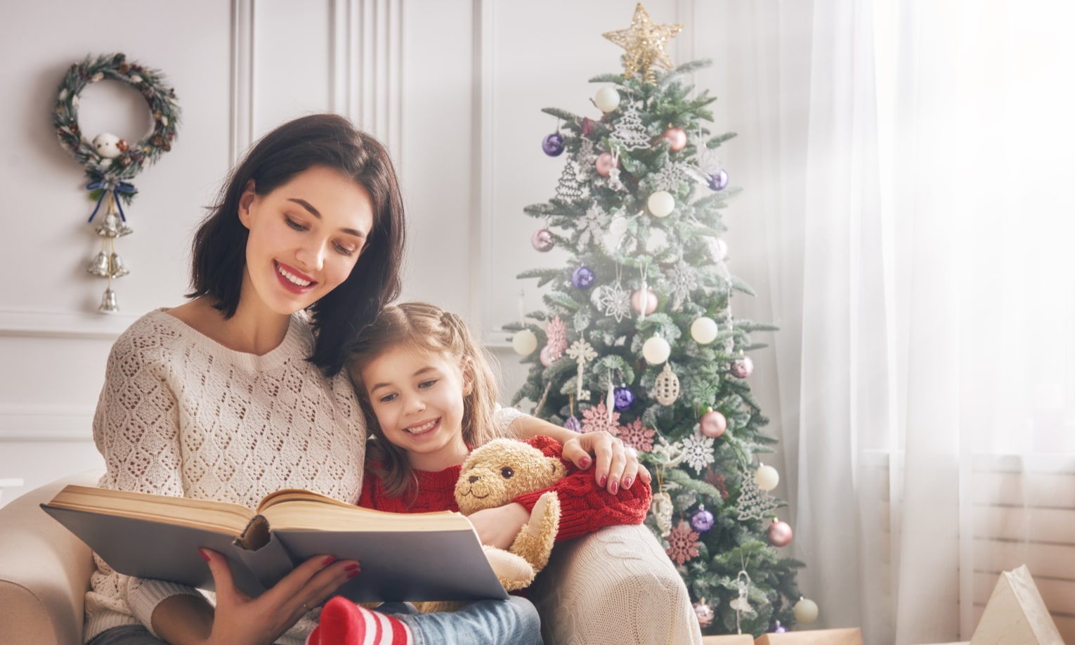 дочь и мама читают книгу у рождественской елки