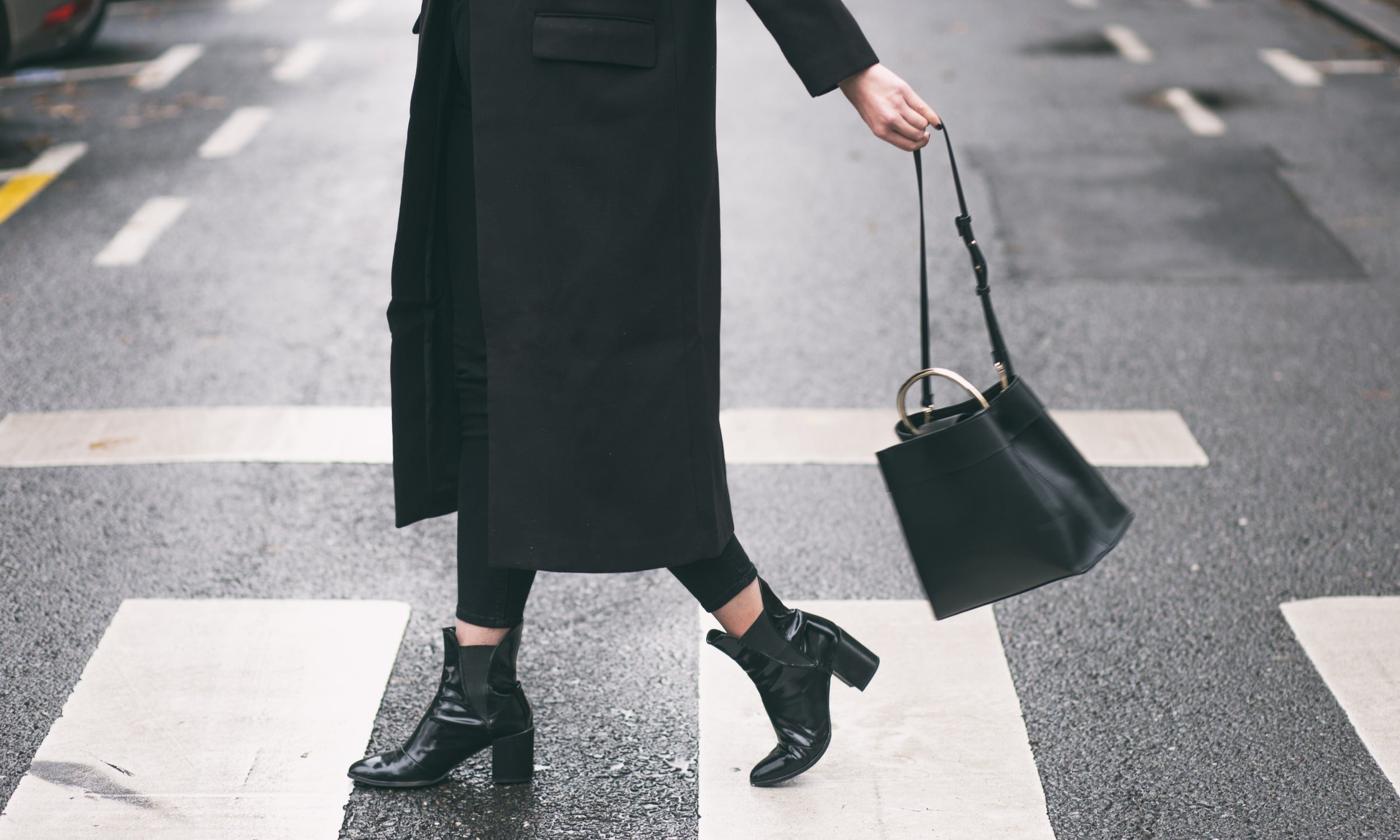 женщина в черном пальто и сумочке идет по улице