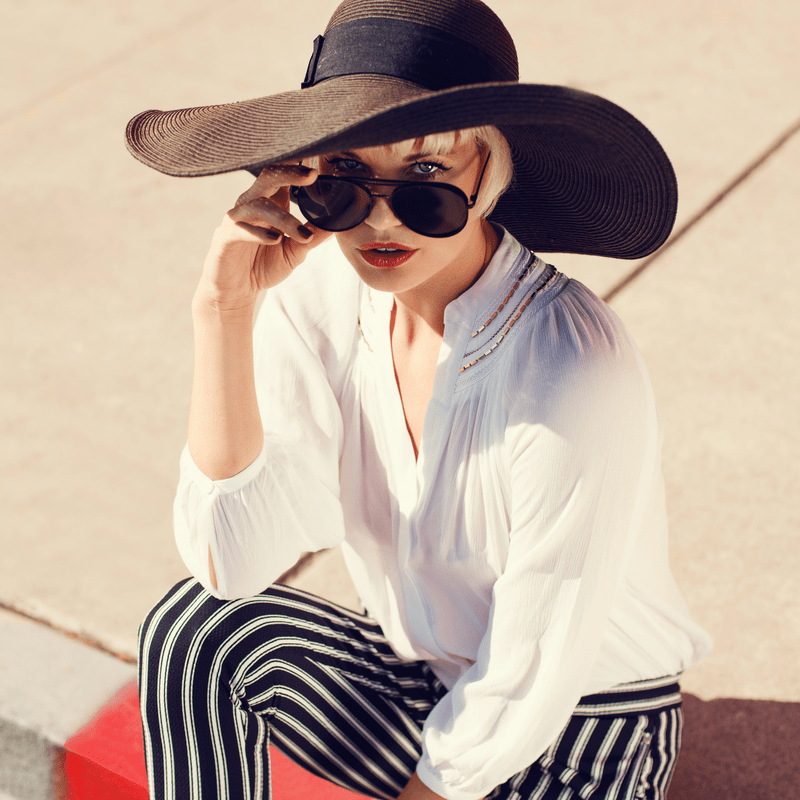 blondine mergina su skrybele ir akiniais nuo saules sedi mieste